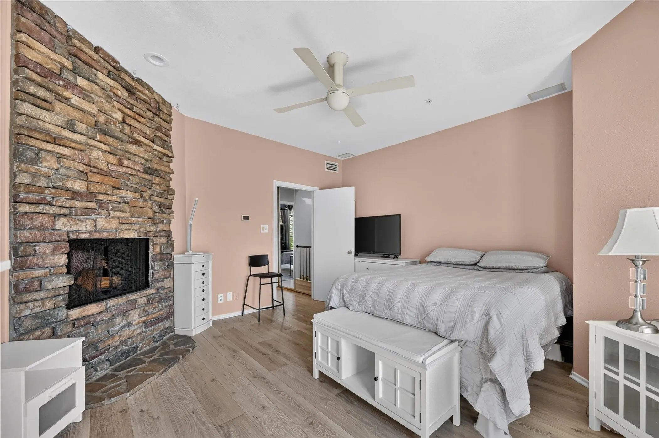 Stone-clad fireplace with a hearth, wood-finish flooring, ceiling fan, and recessed lighting