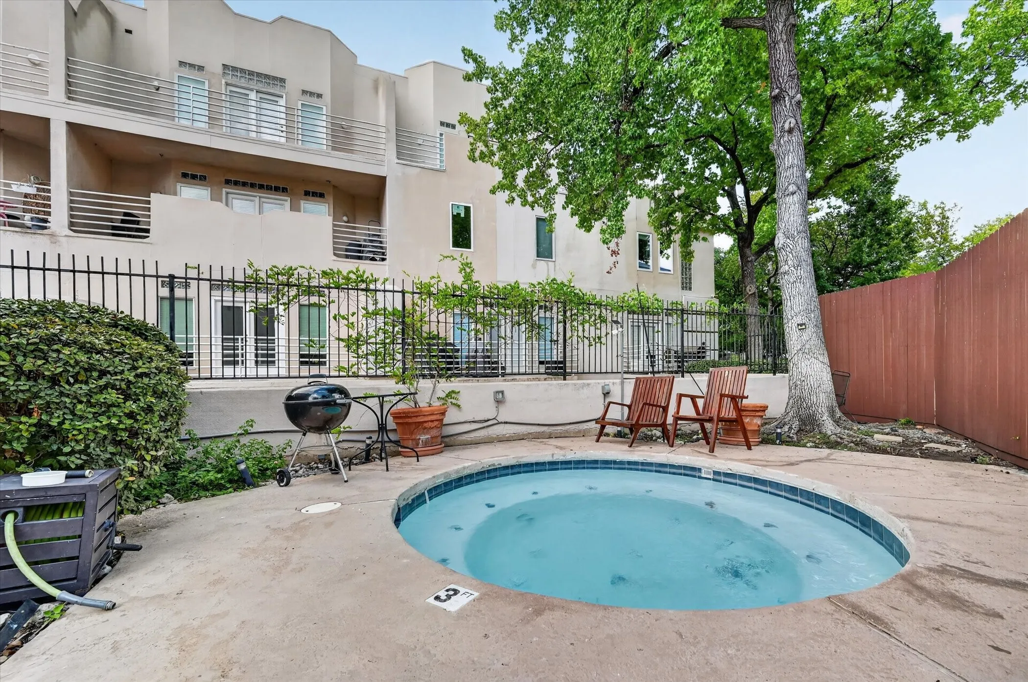 In-ground spa with concrete surround and tiled edge, surrounded by mature trees and a wood fence