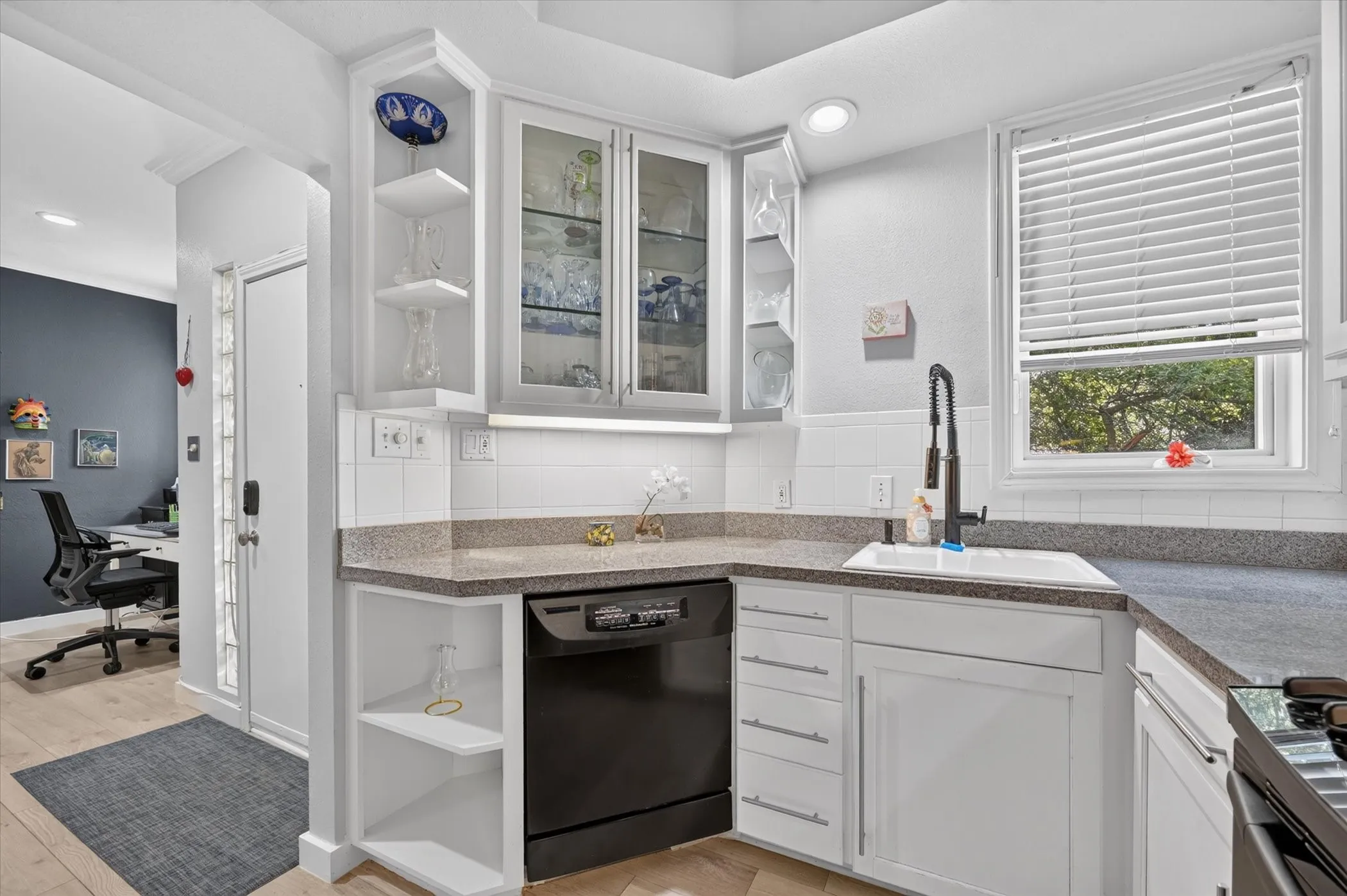White cabinetry with glass-front uppers, solid surface countertops, a white subway tile backsplash, and a built-in black dishwasher