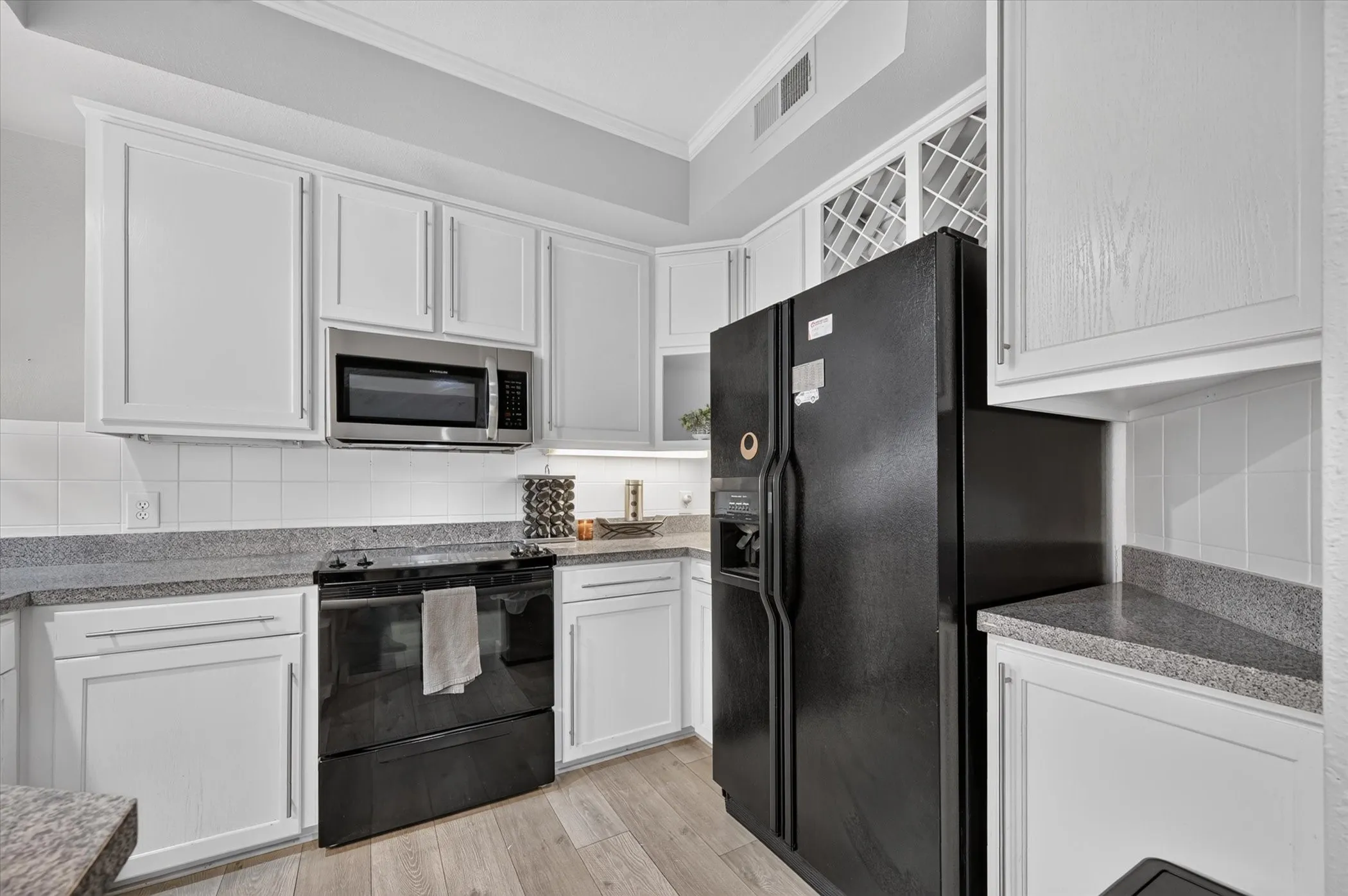 White cabinetry, wood-finish flooring, black appliances, solid surface countertops, and a subway tile backsplash