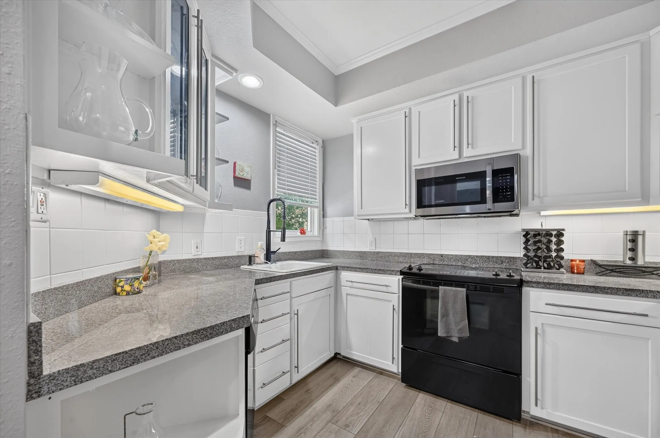 White cabinetry, stainless steel microwave, black electric range, light-toned wood-finish flooring, and grey countertops