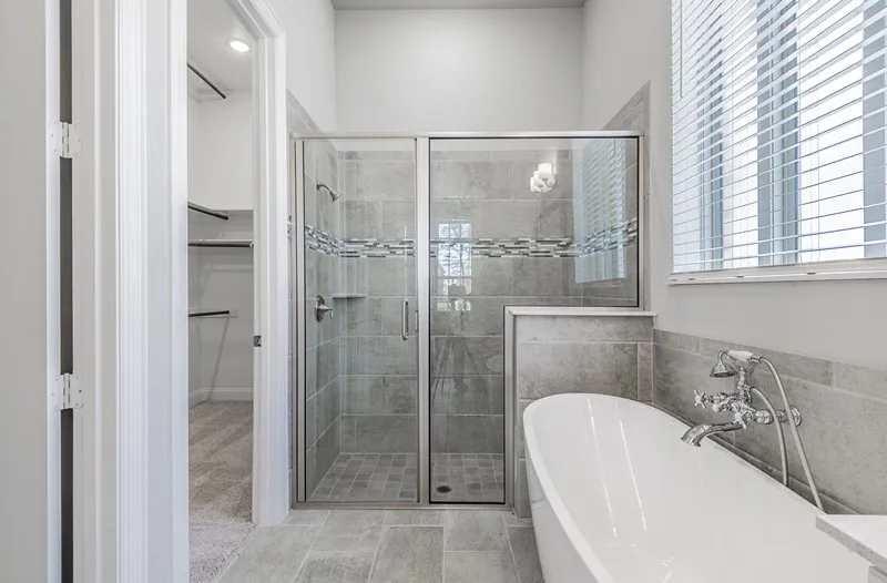 Freestanding bathtub with chrome fixtures, glass-enclosed shower, gray tile flooring, and a walk-in closet with built-in shelving