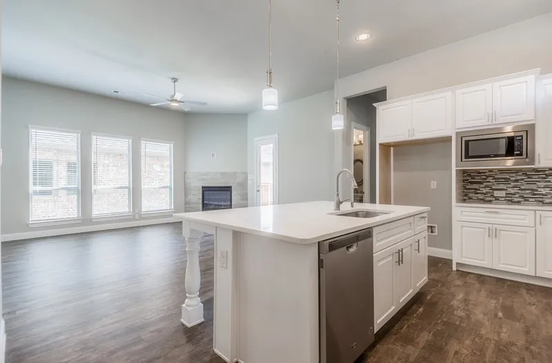 Open concept living space featuring wood-finish flooring, a white kitchen island with an undermount sink, stainless steel dishwasher, and pendant lighting
