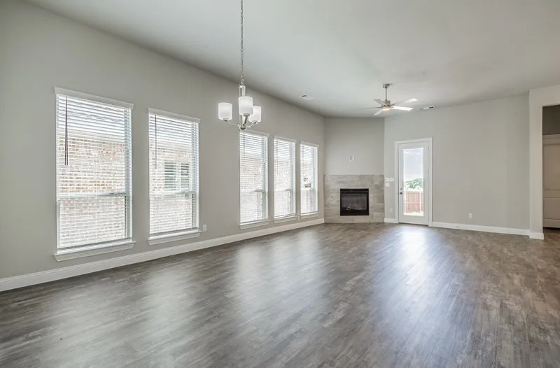 Spacious living area featuring wood-finish flooring, a corner fireplace with stone surround, a ceiling fan, and multiple windows