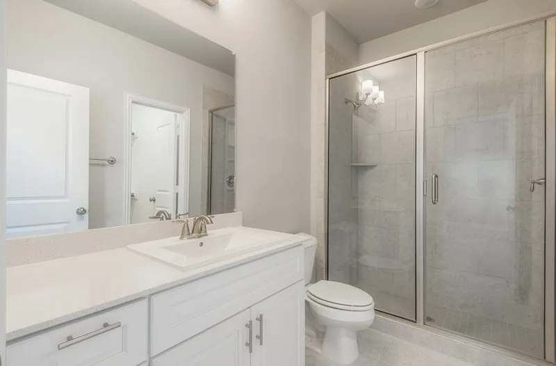 Vanity with integrated sink, sleek countertop, large mirror, glass-enclosed shower, and tiled flooring
