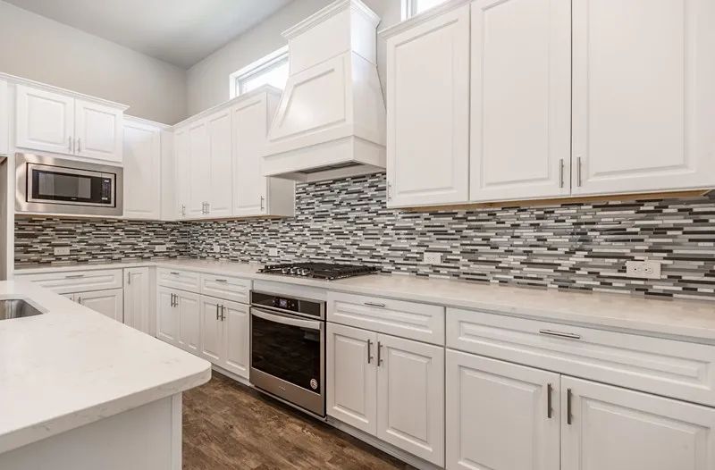 Gourmet kitchen featuring white cabinetry, stainless steel appliances, a built-in microwave, and a decorative tile backsplash