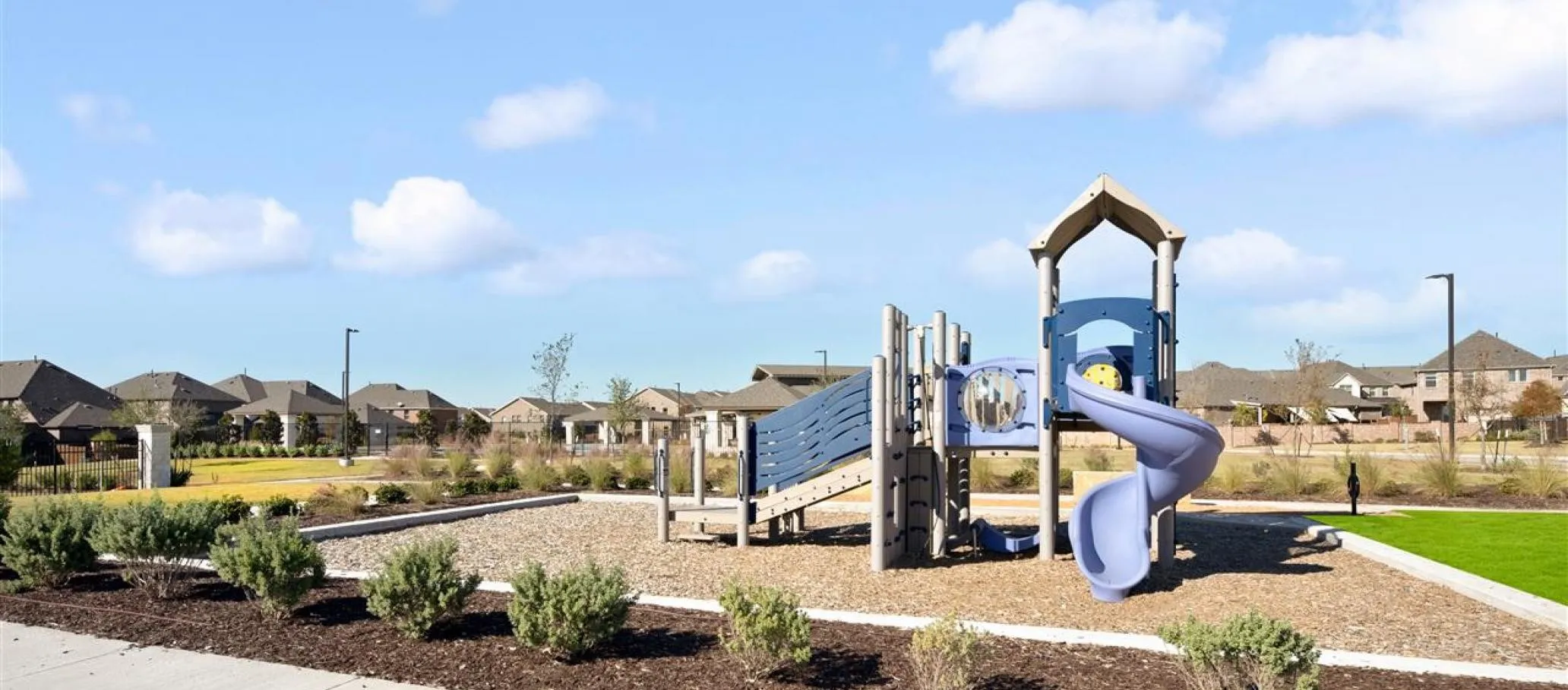 Community playground featuring multiple slides and climbing structures, surrounded by landscaping and residential homes