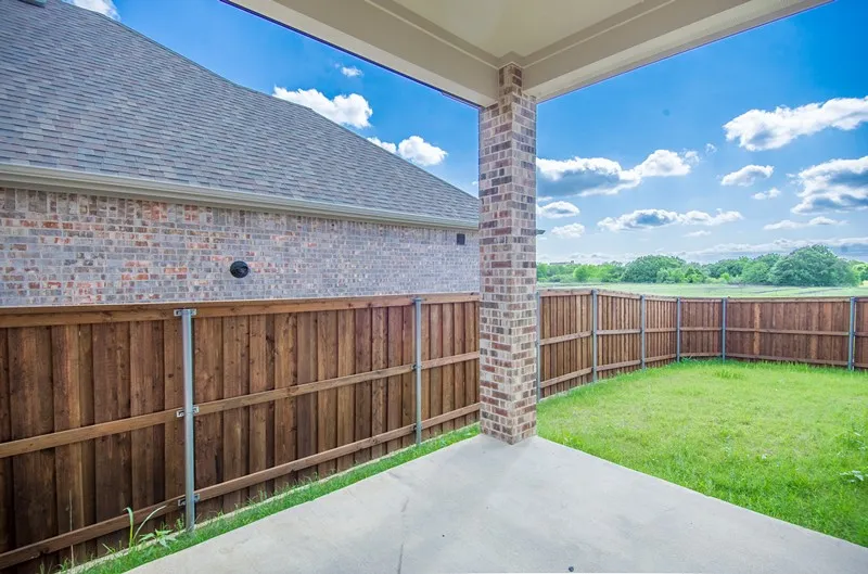 Covered patio with a concrete surface, a brick-clad column, and a wood privacy fence enclosing a grassy yard