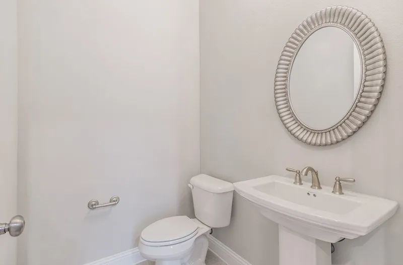 Pedestal sink with brushed nickel faucet, oval framed mirror, and light gray wall paint