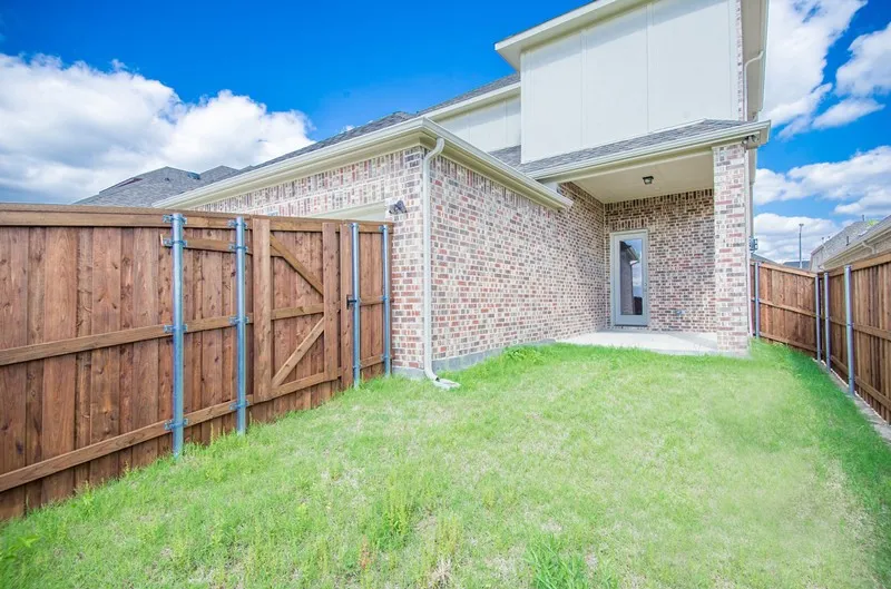 Private backyard featuring a wood privacy fence with gate, brick exterior, and covered patio