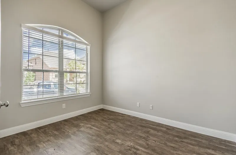 Arched window with blinds, wood-finish flooring, and light-colored wall paint