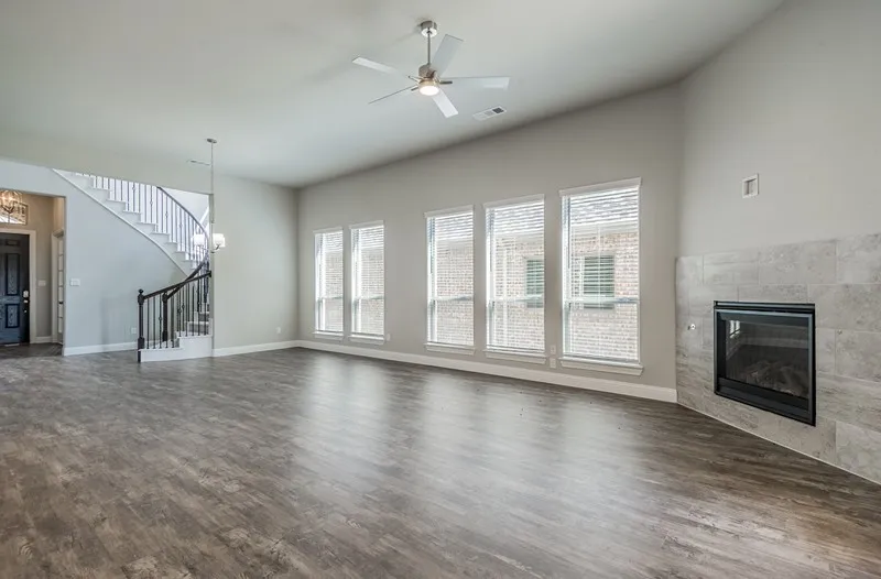 Wood-finish flooring throughout, featuring a curved staircase with wrought iron balusters, a ceiling fan with integrated lighting, a tile-surround fireplace, and multiple windows