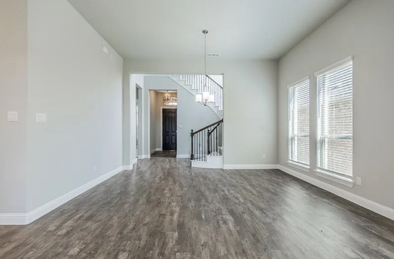 Wood-finish flooring, multiple windows, a staircase with dark wood handrails and white balusters, and a recessed entryway with a dark door