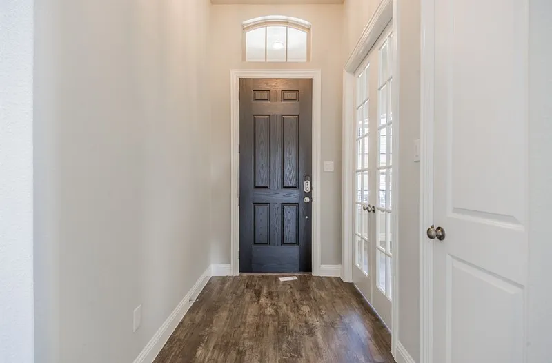 Arched transom window, dark wood-finish entry door, wood-finish flooring, light grey wall paint, and white paneled doors