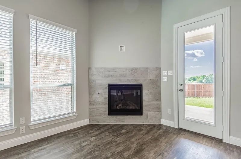 Wood-finish flooring with a tiled fireplace, two windows, and a full-light exterior door
