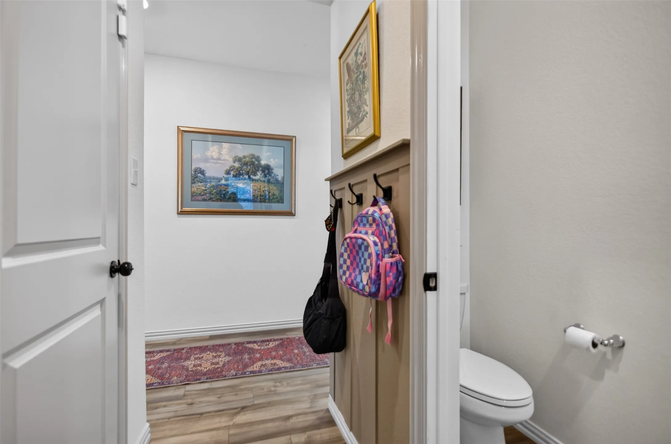 Wood-finish flooring leading to a built-in coat rack with hooks and an adjacent white toilet