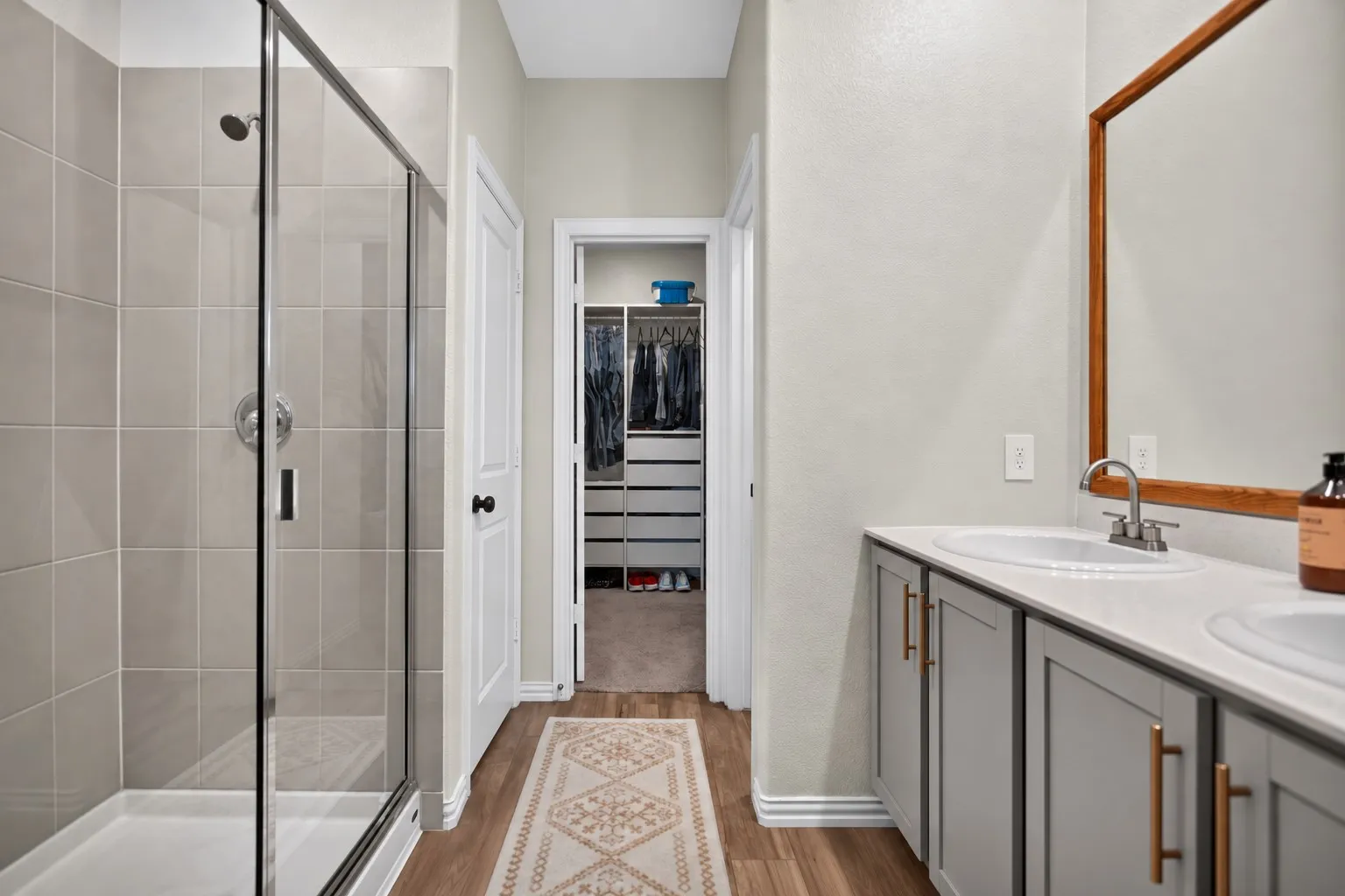 Walk-in shower with clear glass enclosure, dual vanity with undermount sinks, and wood-finish flooring