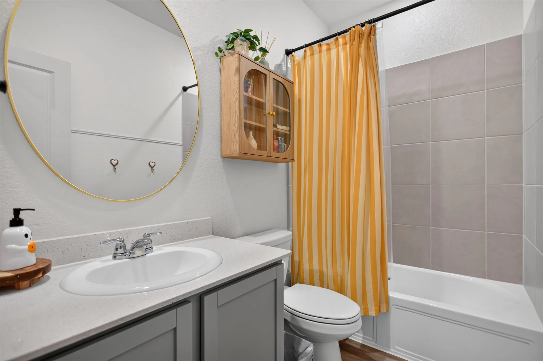 Single vanity with an integrated sink, polished chrome faucet, gray cabinetry, and a round gold-framed mirror