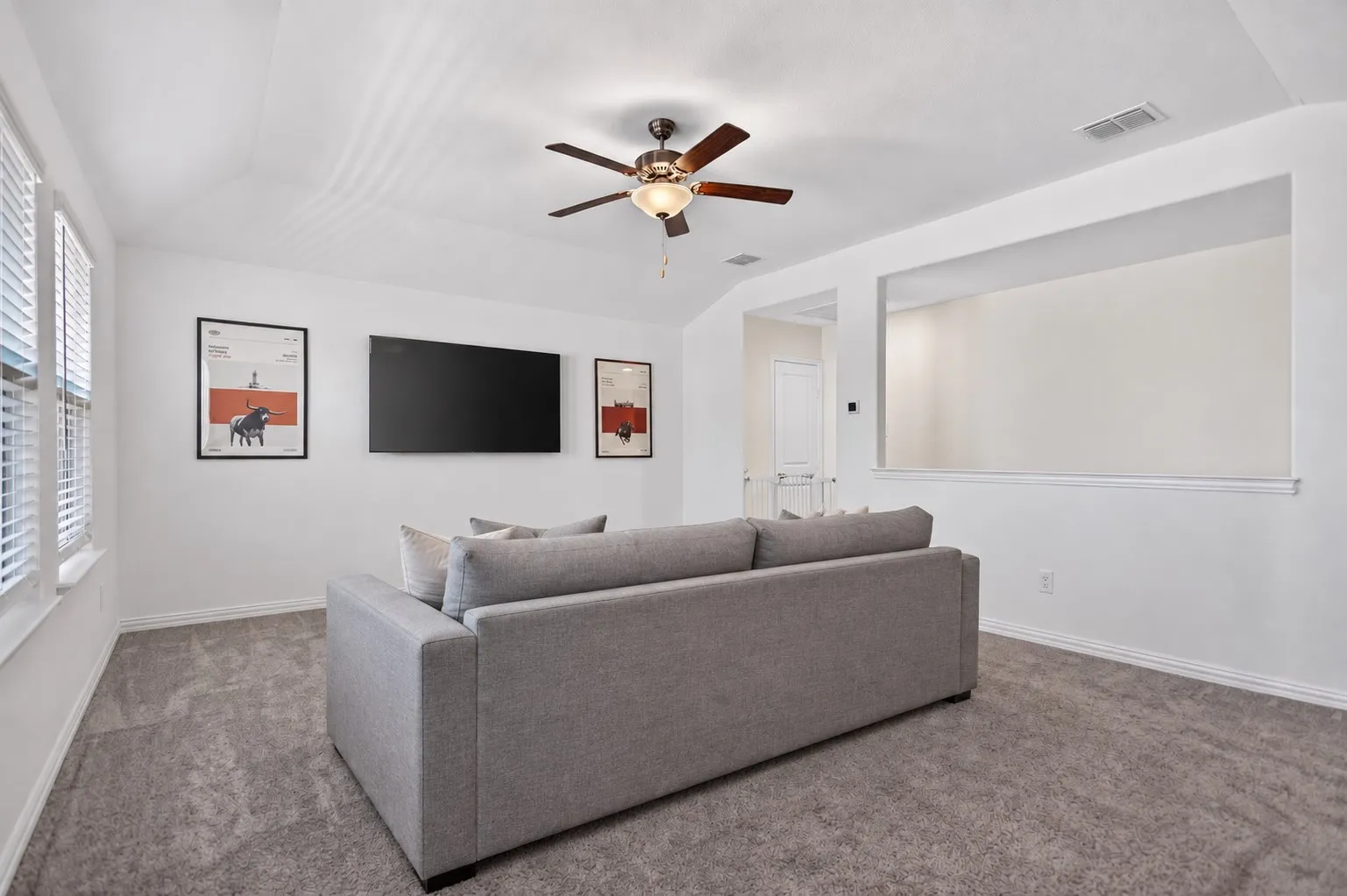 Vaulted ceiling with a ceiling fan, carpeted flooring, and a wall-mounted display
