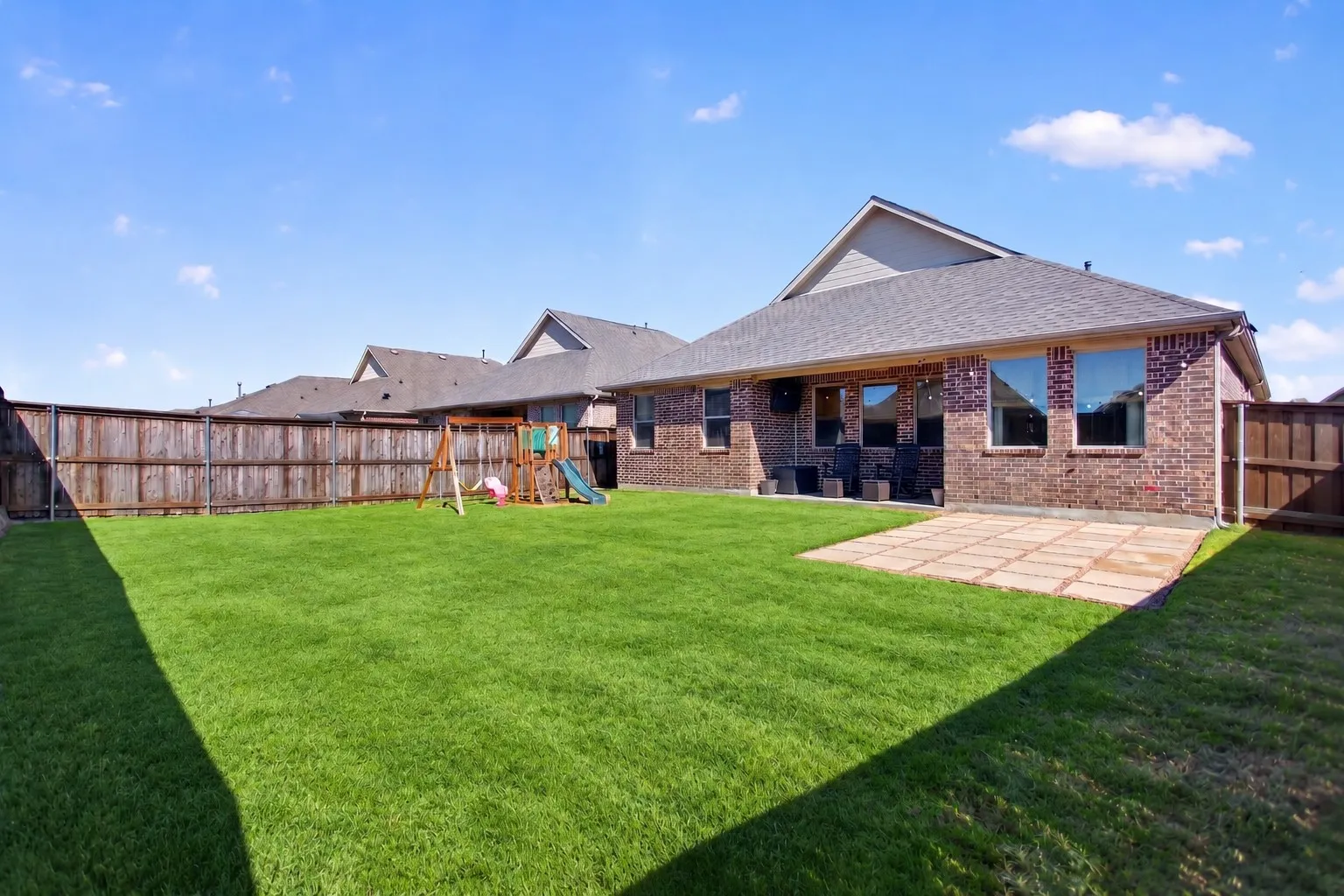 Expansive backyard featuring a manicured lawn, wood privacy fencing, and a paver patio