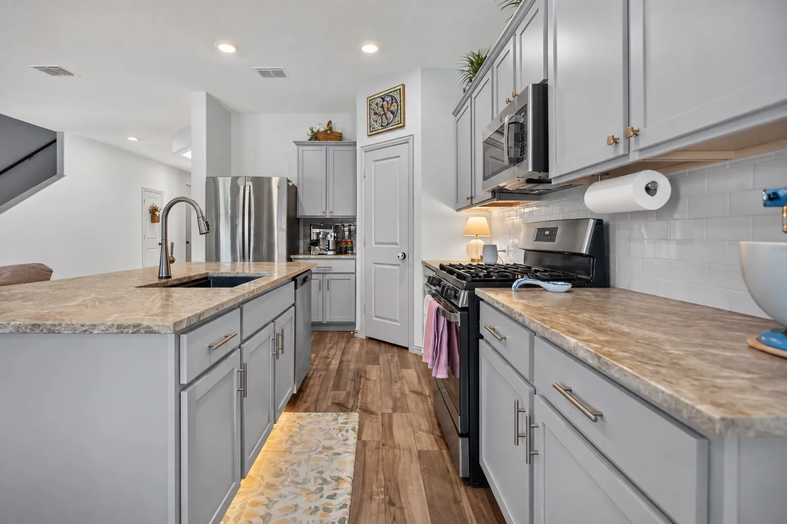 Kitchen featuring a stainless steel range, microwave, and refrigerator, light gray cabinetry, wood-finish flooring, and a subway tile backsplash
