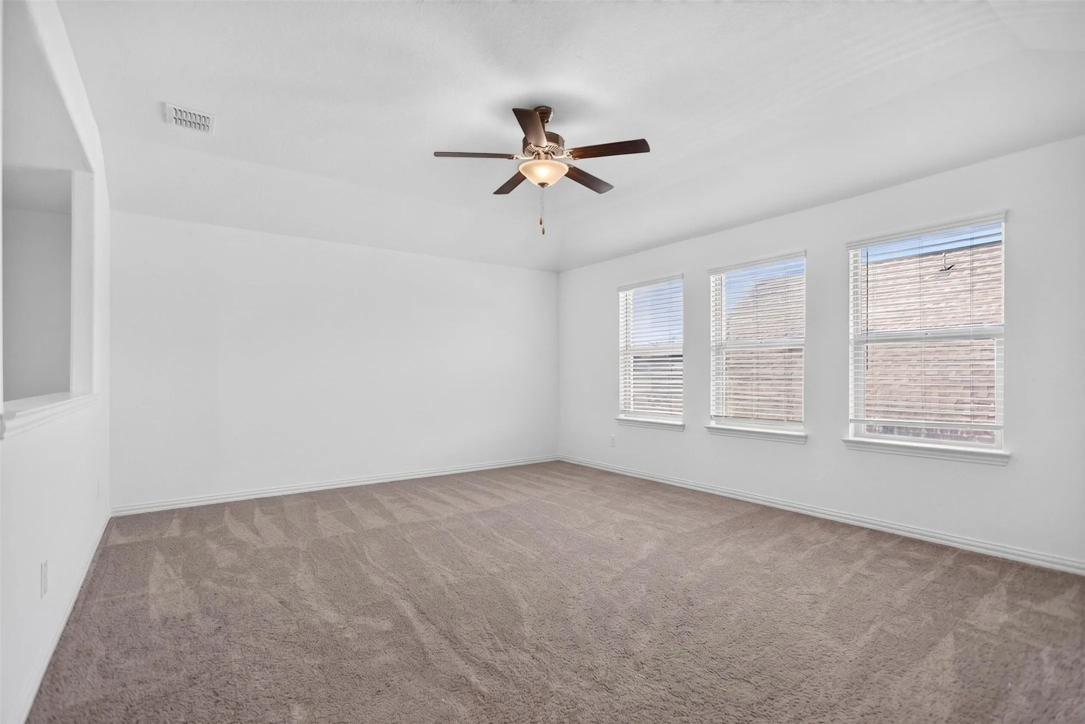Spacious room with plush carpeting, triple windows with blinds, a ceiling fan, and crisp white walls