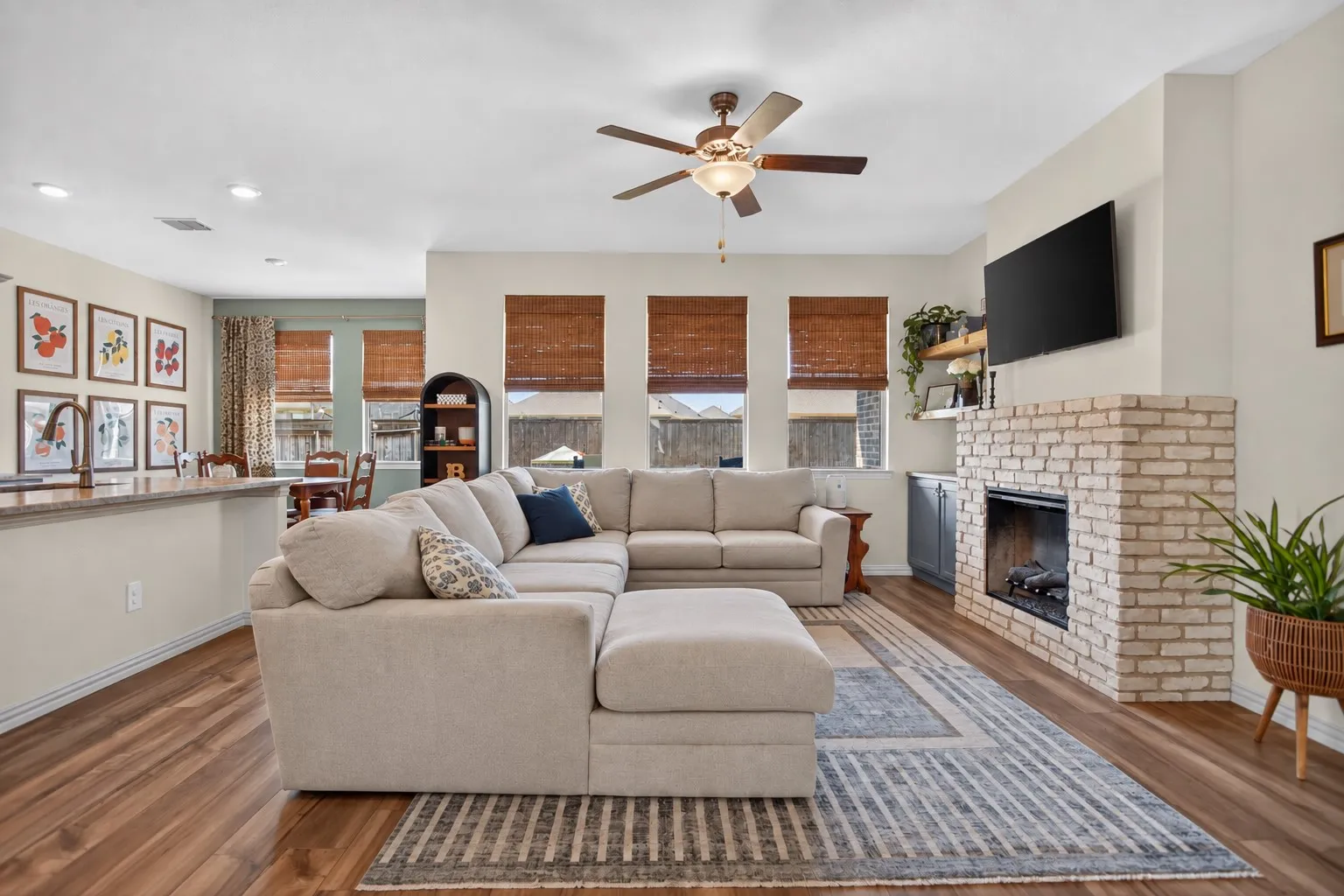 Wood-finish flooring, ceiling fan, brick-clad fireplace, built-in shelving, and recessed lighting