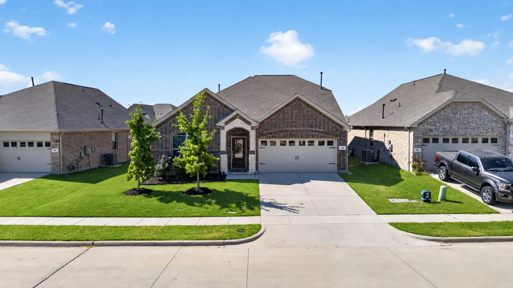 Brick and stone exterior with a two-car garage, manicured lawn, and concrete driveway