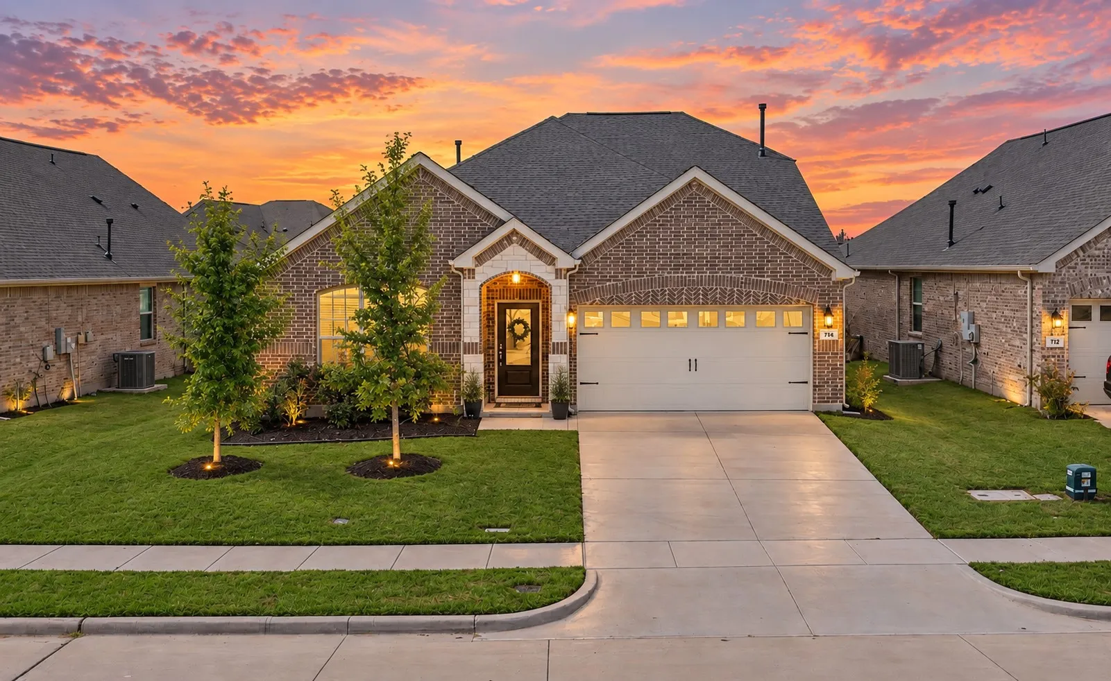 Brick and stone facade residence featuring an attached two-car garage, concrete driveway, and a landscaped front yard with established trees