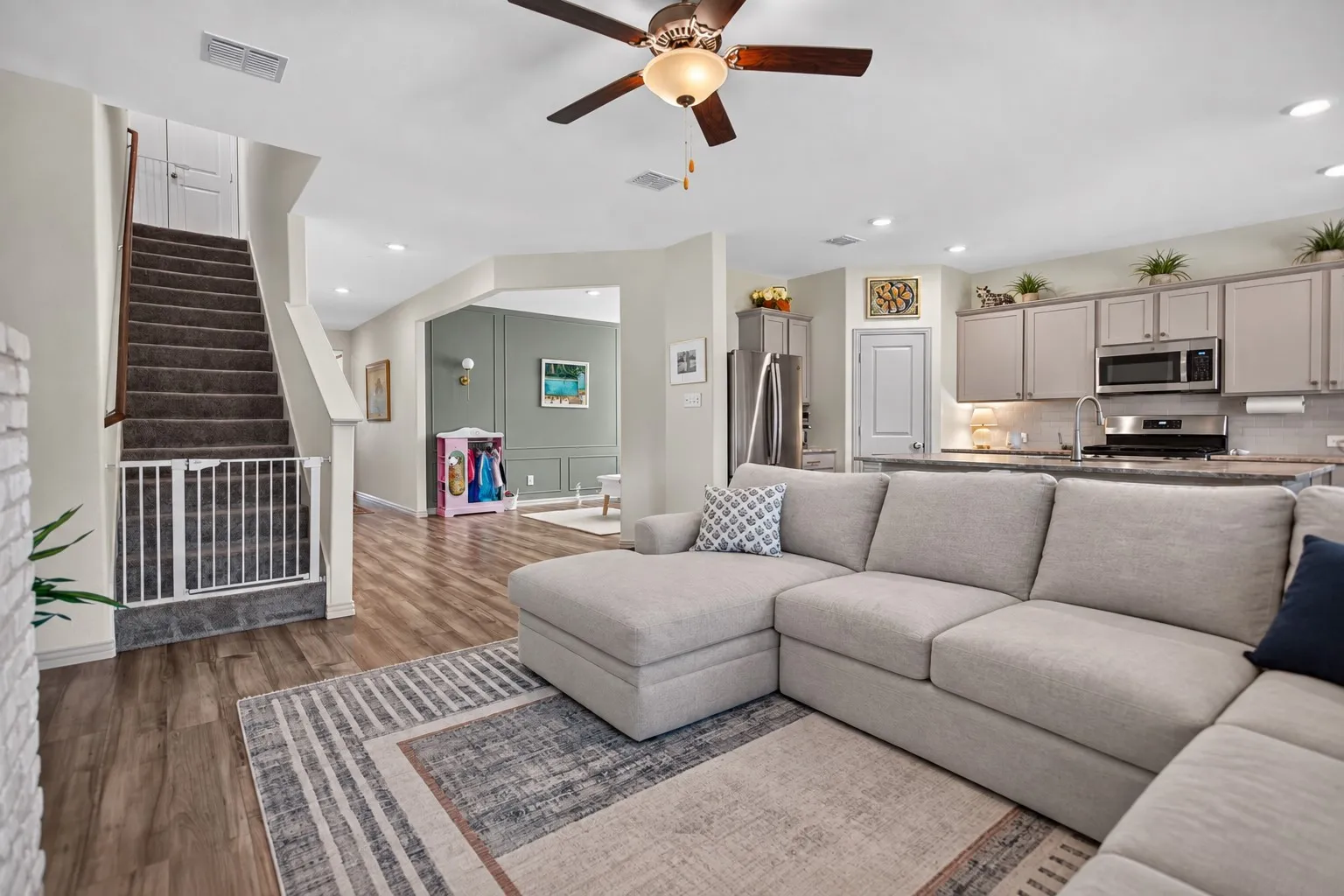 Open-concept living area featuring wood-finish flooring, a ceiling fan, recessed lighting, and a kitchen with stainless steel appliances