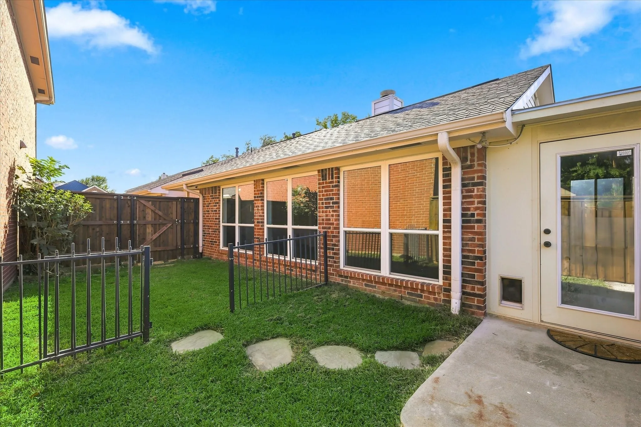 Private backyard with a concrete patio, stepping stones, and a partial black metal fence