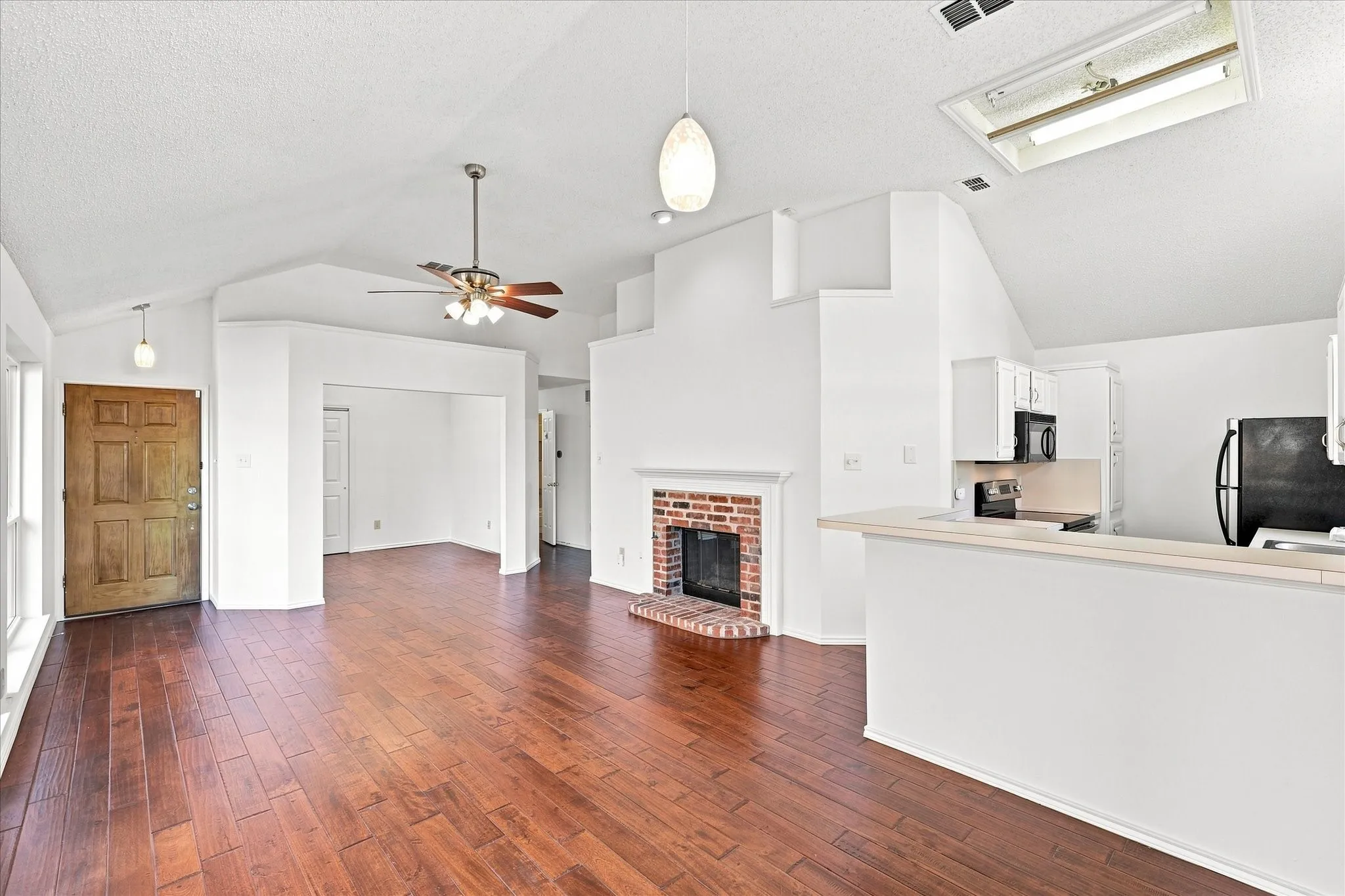 Vaulted ceilings, engineered hardwood flooring, brick fireplace, kitchen with white cabinetry, and a skylight