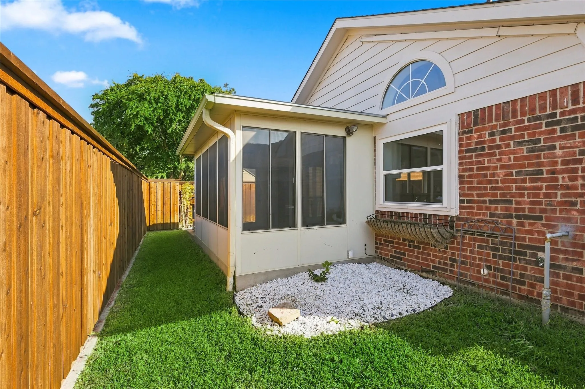Screened-in patio with multiple windows, brick exterior, arched window detail, and a wood privacy fence