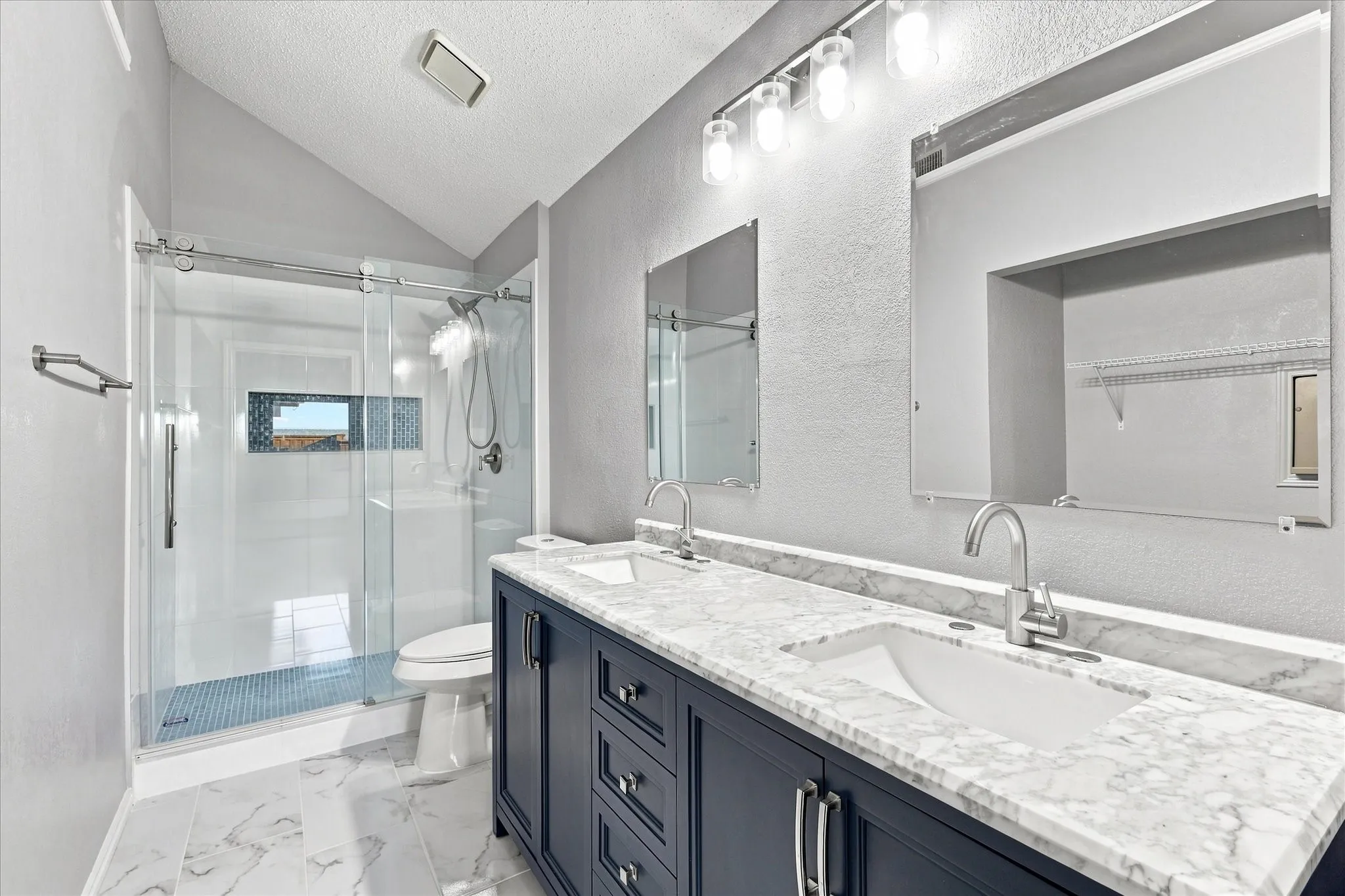 Upgraded primary bathroom with dual vanity with undermount sinks and stone finish countertops