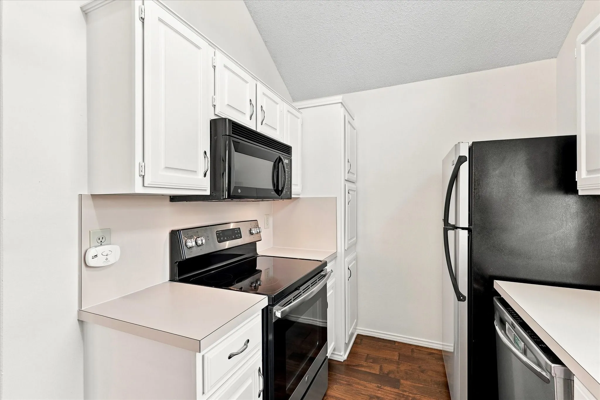 White shaker-style cabinetry, black and stainless steel appliances, laminate countertops.