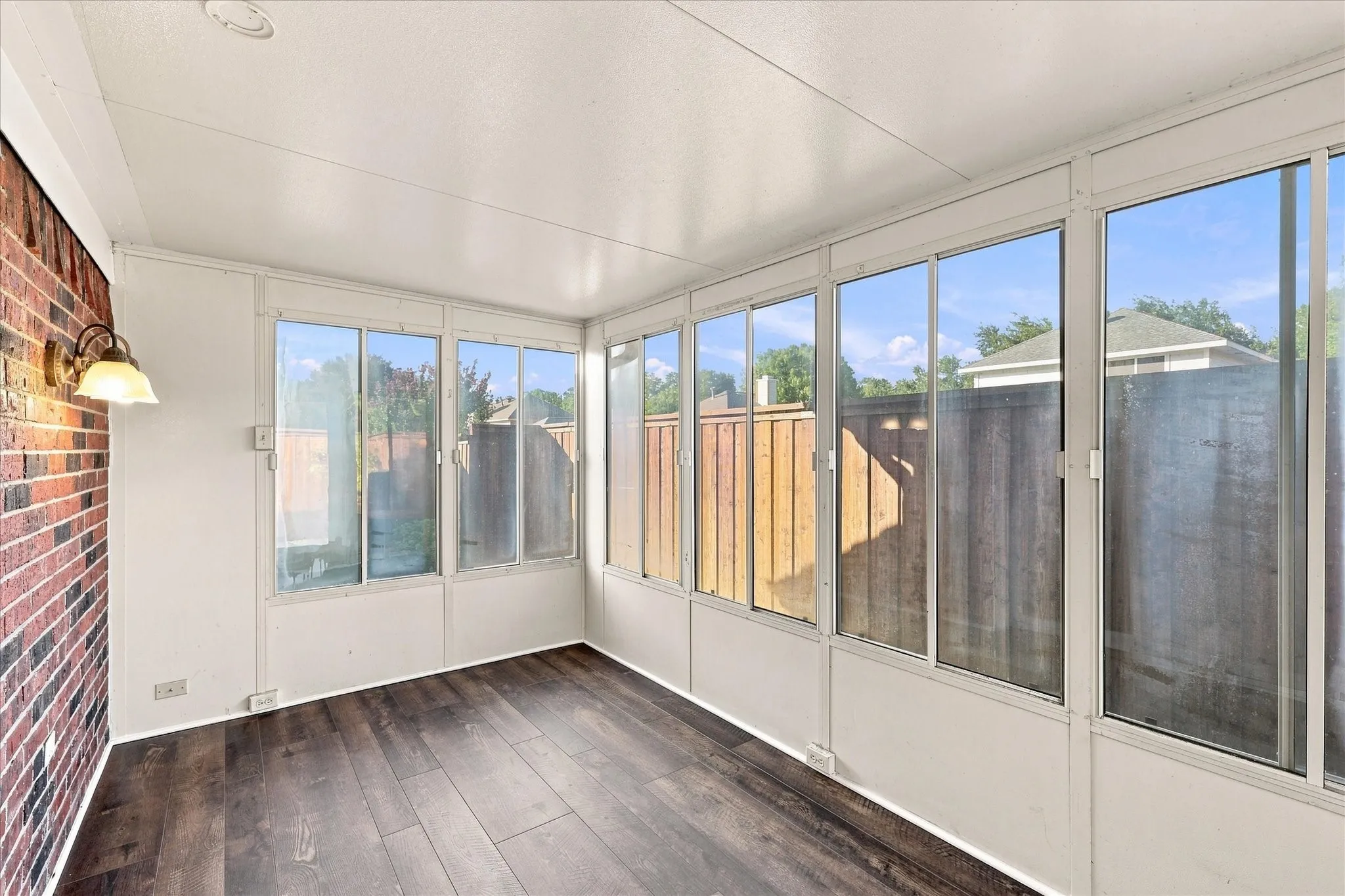 Sunroom featuring extensive window panels, LVP flooring and a brick accent wall with a wall-mounted light fixture and a/c unit.