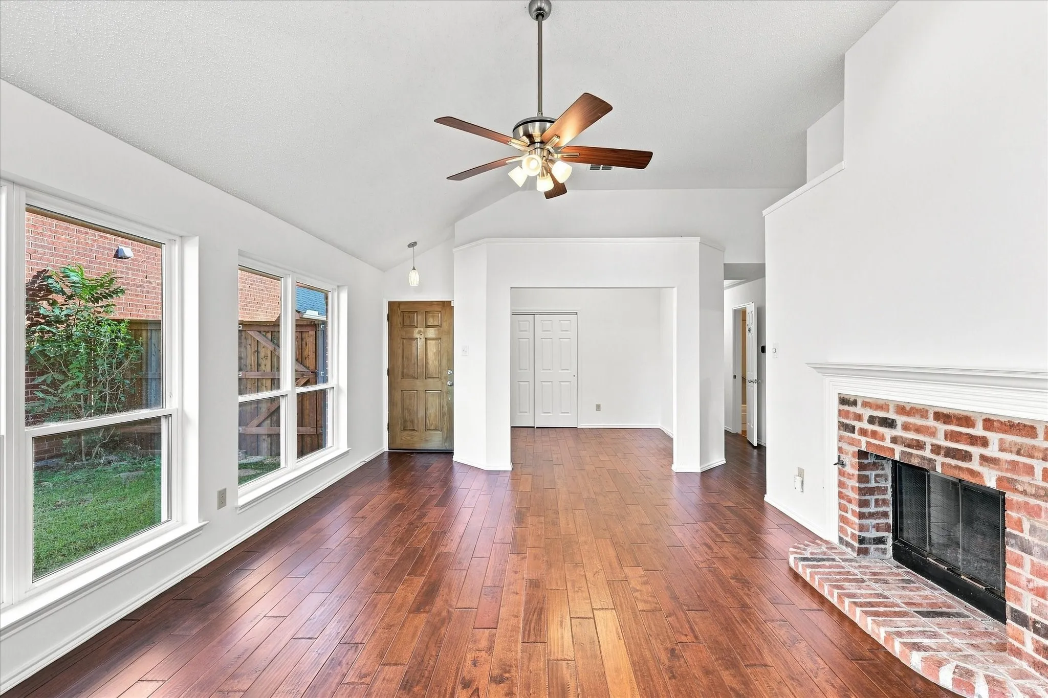 Vaulted ceiling with a ceiling fan, engineered hardwood flooring, brick fireplace, and multiple windows w/flex-office room
