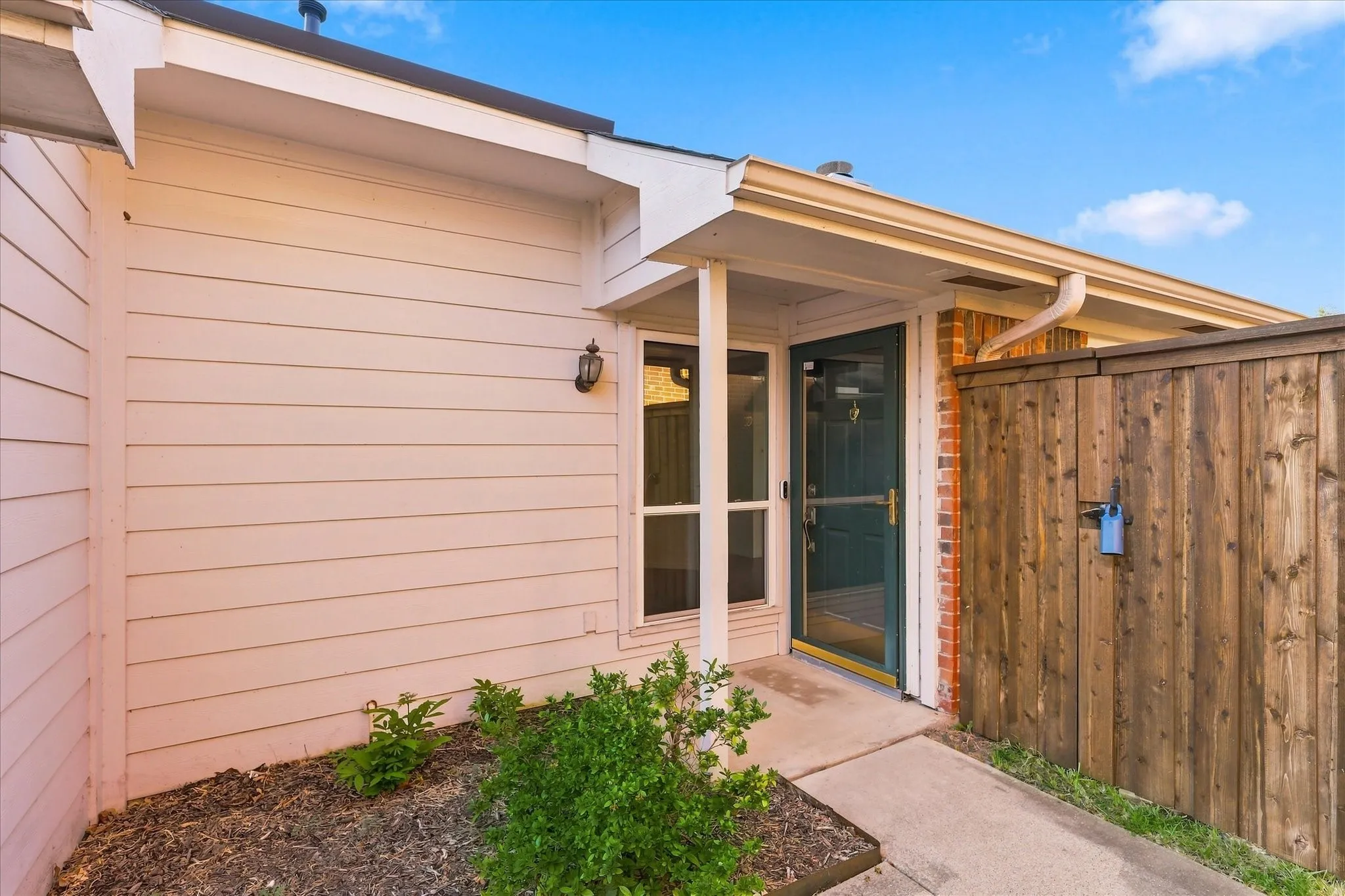Covered entryway featuring a storm door, brick facade, and wood siding