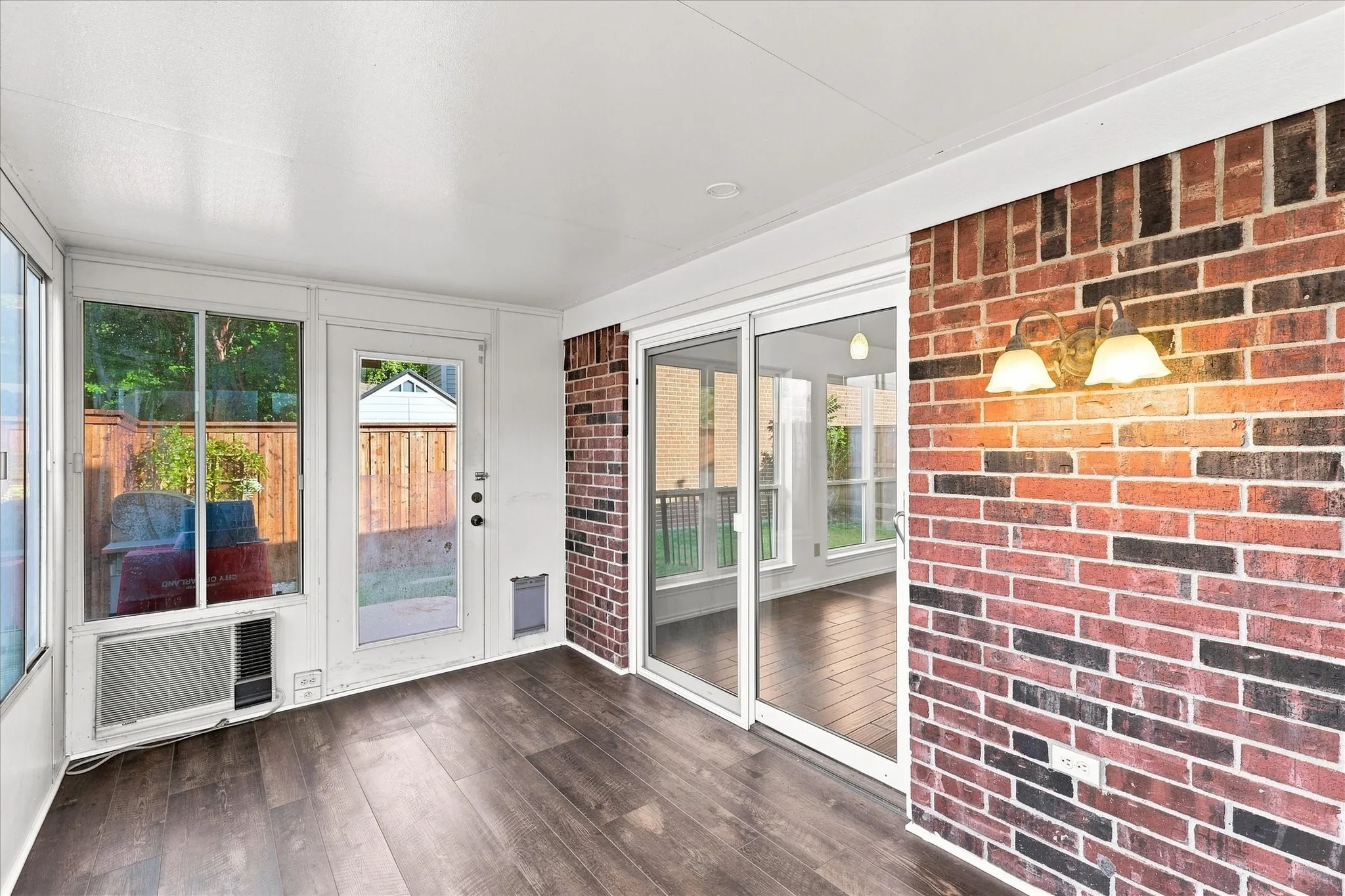 Enclosed porch with LVP flooring, brick accent wall, sliding glass doors, and white paneled windows