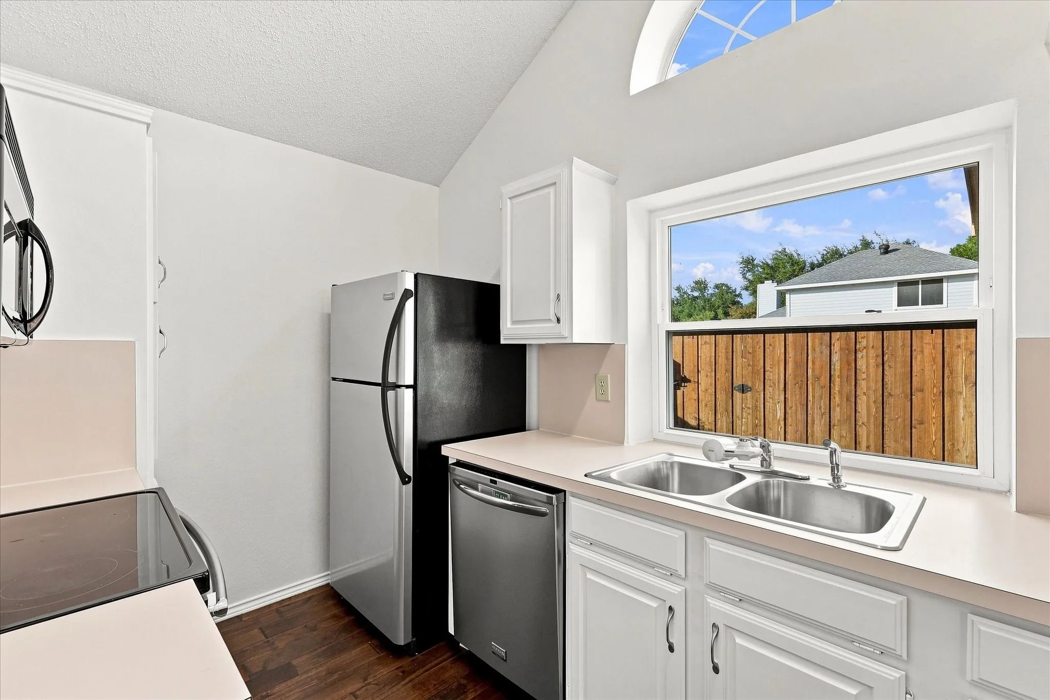 Vaulted ceilings, white cabinetry, dual basin stainless steel sink, and arched window