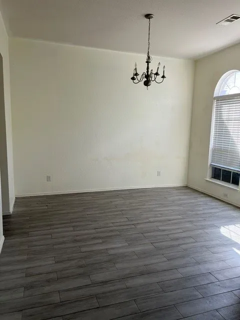 Wood-finish tile flooring, arched transom window, window blinds, and a suspended chandelier