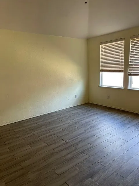 Wood-finish tile flooring throughout, featuring neutral wall tones and multiple windows with horizontal blinds