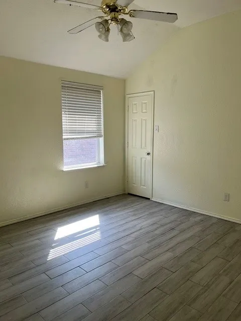 Vaulted ceiling with a ceiling fan, window with blinds, paneled door, and wood-finish tile flooring