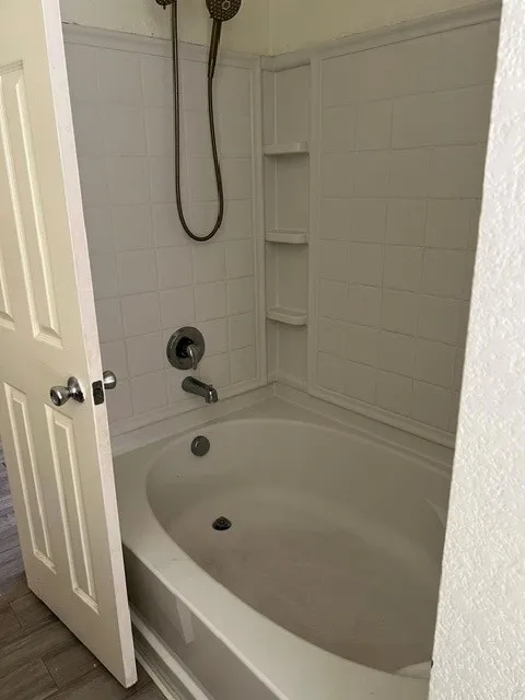 Bathtub with integrated shelving, chrome fixtures, and a handheld shower head