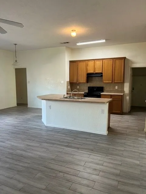 Kitchen island with integrated sink, wood-finish cabinetry, tile flooring, and a ceiling fan