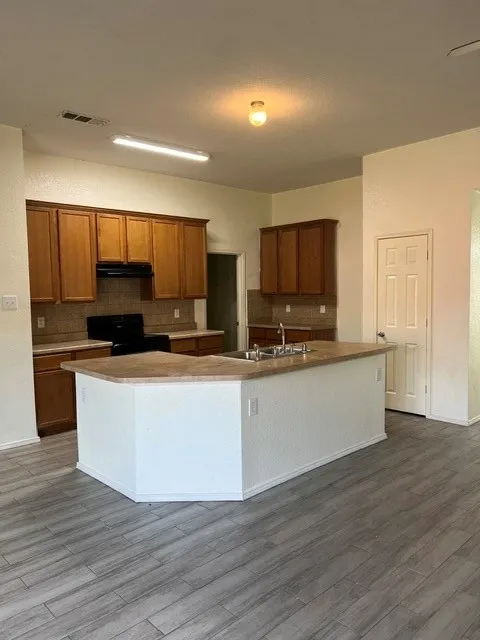 Kitchen featuring wood-finish cabinetry, a central island with integrated sink, and tile flooring