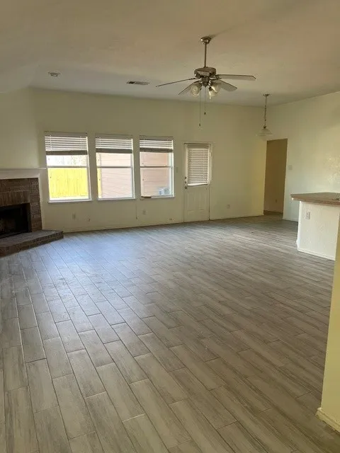Spacious living area featuring wood-finish tile flooring, a brick fireplace, vaulted ceilings, and a ceiling fan with integrated lighting