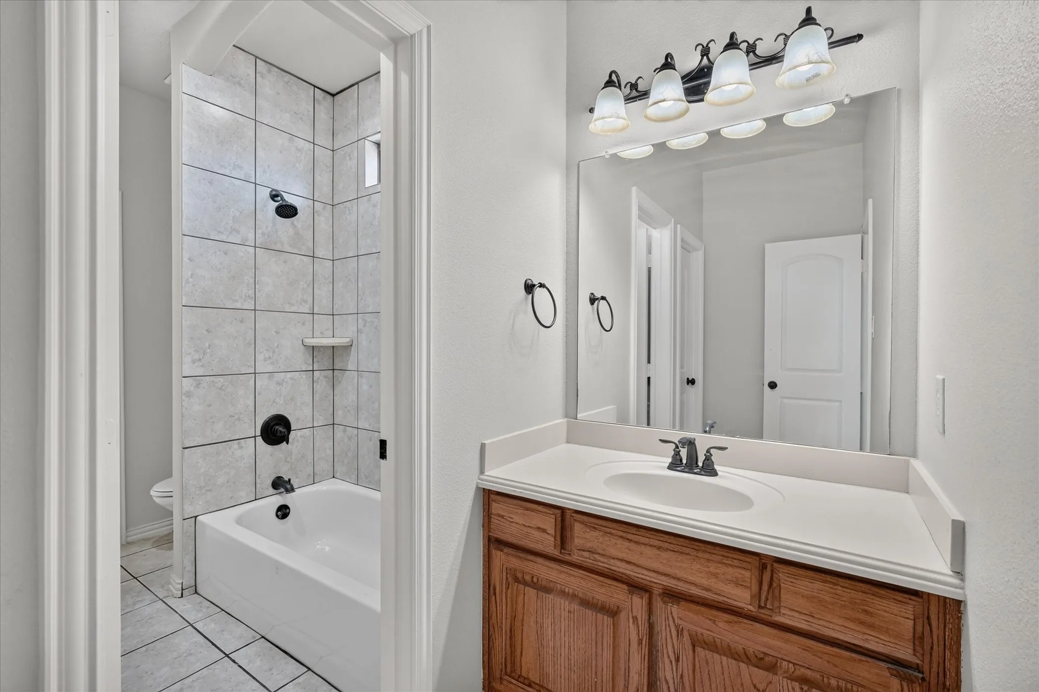 Vanity with wood-finish cabinetry, white countertop with integrated sink, and an overhead light fixture
