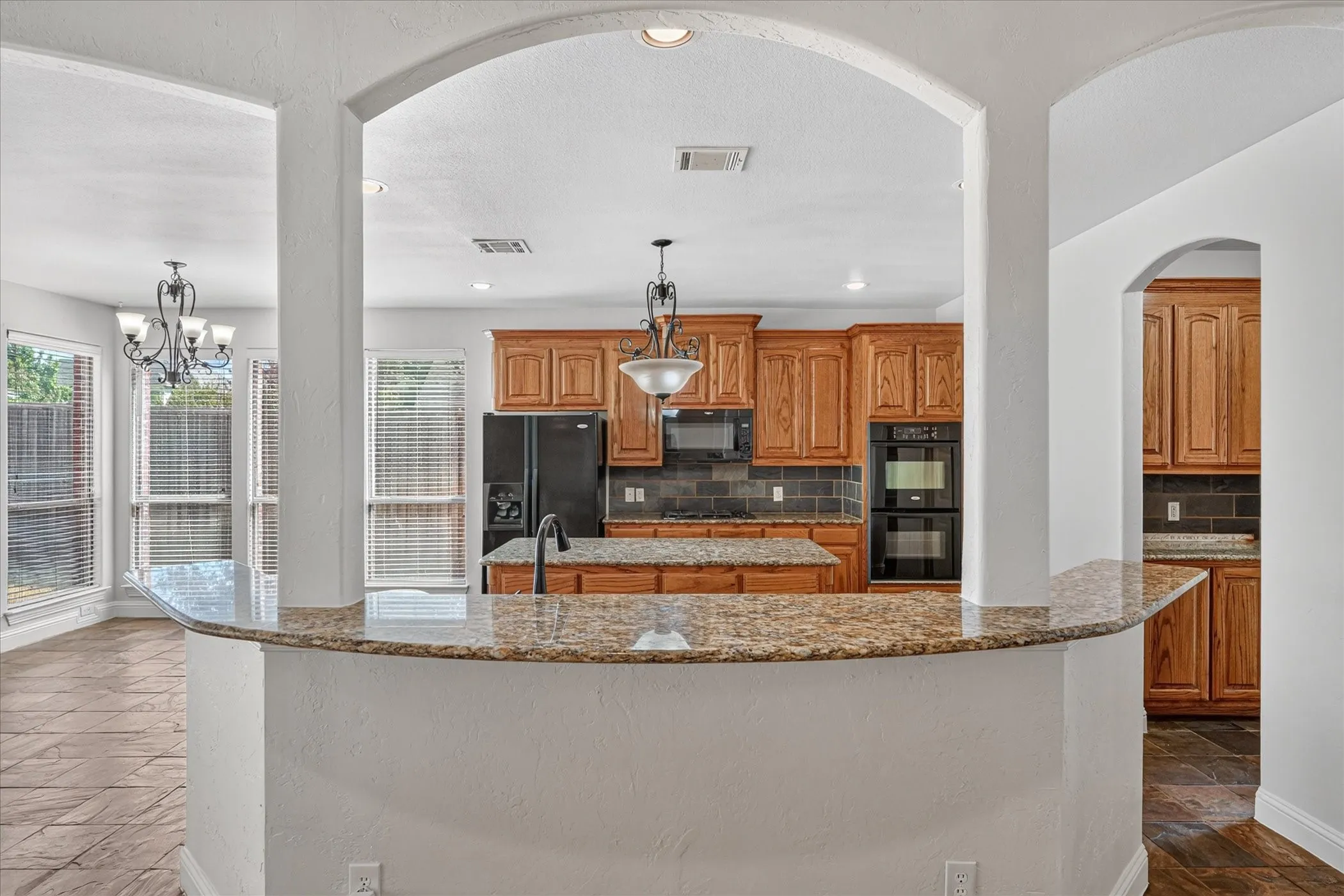 Kitchen with wood cabinetry, granite countertops, black appliances, and a tile backsplash