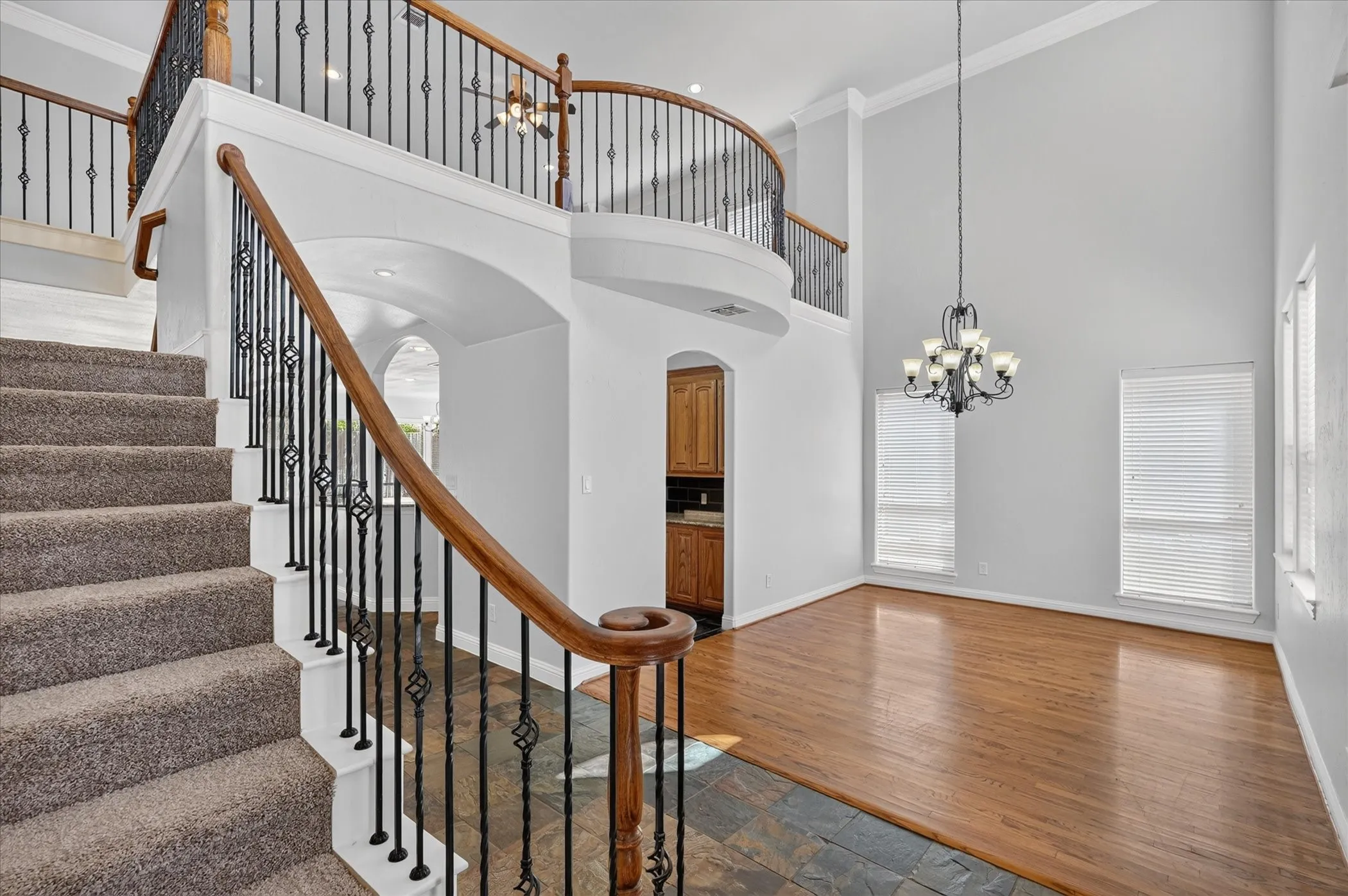 Two-story foyer featuring a curved staircase with wrought iron balusters and wood handrails, double-height ceilings, a decorative chandelier, and wood-finish flooring